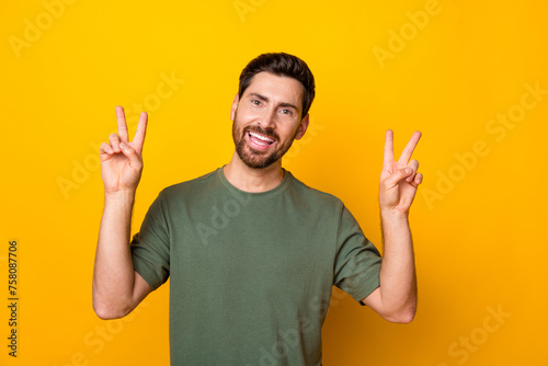 Photo of positive funky guy dressed green t-shirt showing two v-signs isolated yellow color background