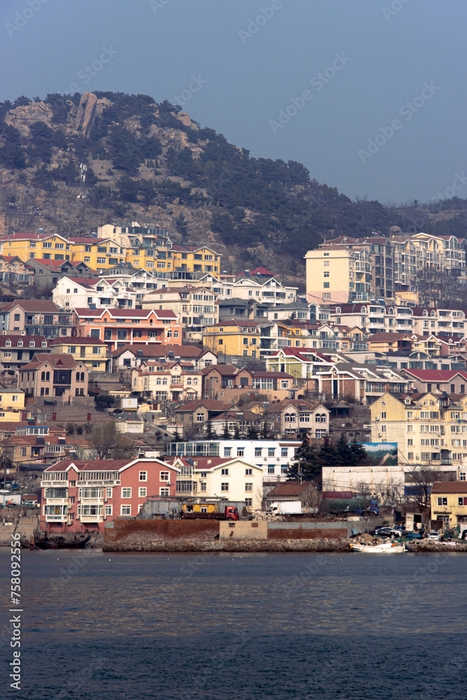 Landscape of Shazikou fishing village in Qingdao, Shandong, China, with colorful residential buildings and Laoshan Mountain in the background