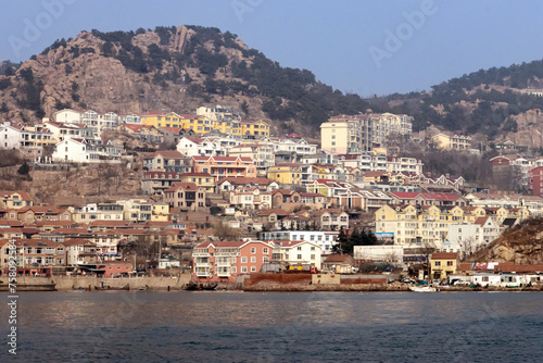 Landscape of Shazikou fishing village in Qingdao, Shandong, China, with colorful residential buildings and Laoshan Mountain in the background