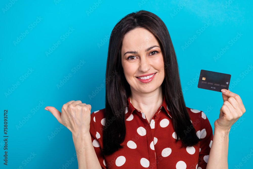 Photo portrait of attractive woman hold credit card point empty space dressed stylish dotted red clothes isolated on blue color background Photo portrait of attractive woman hold credit card point empty space dressed stylish dotted red clothes isolated on blue color background