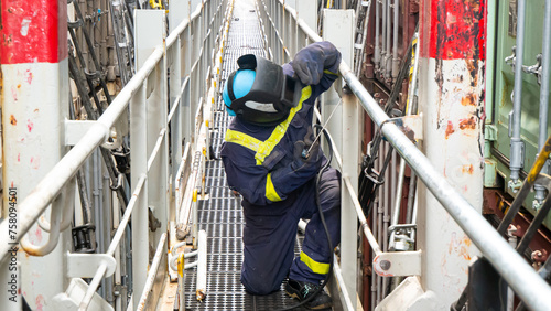 Seaman crew member fitter welder of cargo vessel is repairing ship structure lashing bridge by welding of new pipes dressed with proper ppe