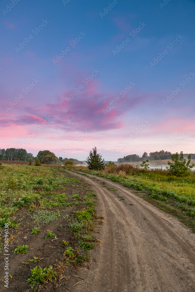 A rural landscape with a road extending into the distance. Dawn, early morning. Beautiful sky with bright red clouds.