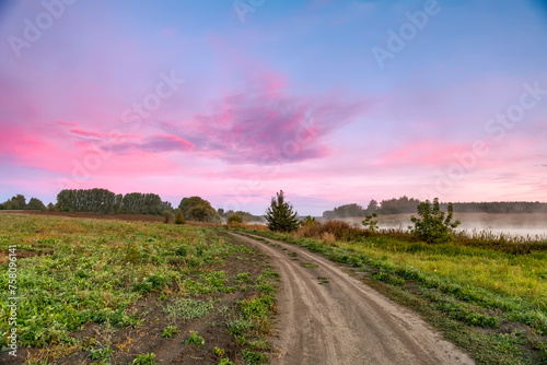 A rural landscape with a road extending into the distance. Dawn, early morning. Beautiful sky with bright red clouds.