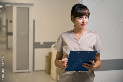 Female medical worker holding clipboard standing in hospital hallway