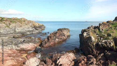 Peaceful view of the waves gently rolling into the rocky foreshore at Crawfordsburn Country Park on a beautiful summer morning with light winds and a blue sky photo