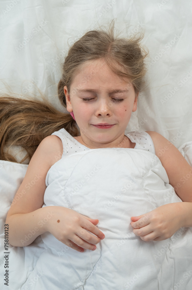 Top view of a little dissatisfied girl lying in bed. Vertical photo. Top view of a little dissatisfied girl lying in bed. Vertical photo.