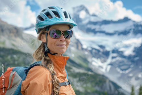 Woman wearing helmet and sunglasses glasses stands confidently before towering mountain backdrop ready for adventure, exploration.She may be gearing up for bicycle ride or some other outdoor activity © Nataliia_Trushchenko