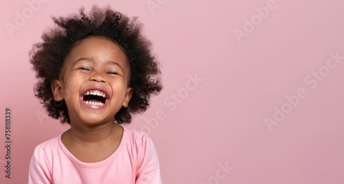 Portrait of a cute African American baby girl laughing on pink background