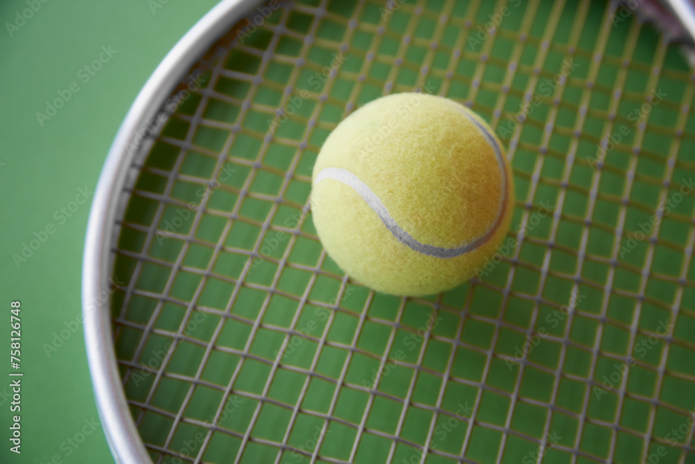 A yellow tennis ball lies on a tennis racket on a green  background