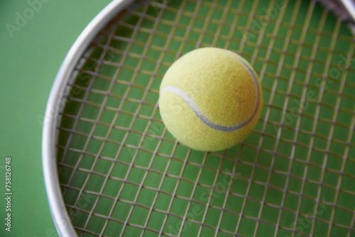 A yellow tennis ball lies on a tennis racket on a green background