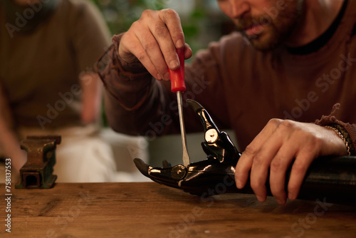 Selective focus closeup of engineer sitting at wooden table repairing prosthetic arm with use of screwdriver photo