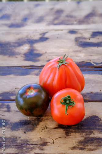 Raw tomatoes of three different varieties, on a wooden table.