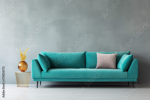 A blue couch sits in front of a wall with a greyish color. A vase with yellow flowers sits on a table in front of the couch. The couch is the main focus of the image