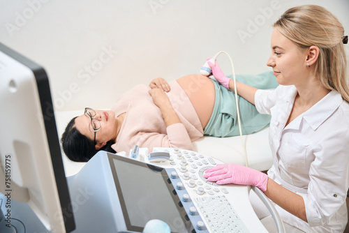 Smiling woman gynecologist making ultrasound of woman on second trimester photo