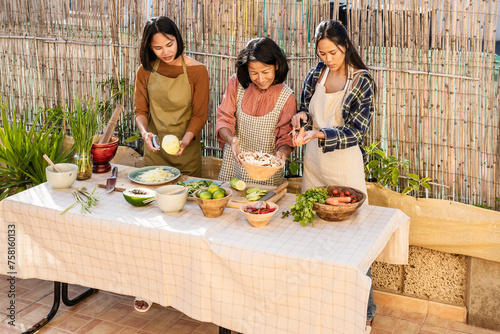 Southeast Asian mother and her daughters are having fun cooking a Thai food recipe together in the backyard