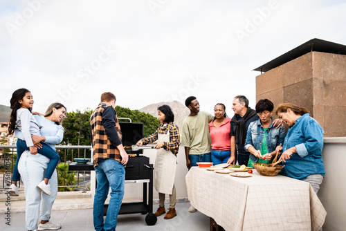 Multigenerational friends having fun doing barbecue at house rooftop - Happy multiracial people cooking together