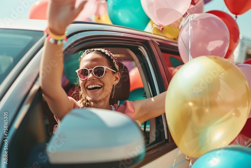 A joyful young woman waving from the window of a car, adorned with colorful balloons, setting off for a fun-filled holiday journey photo