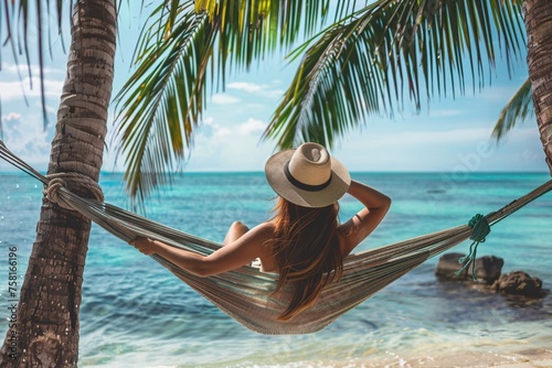 Captivating woman reclining in a hammock strung between two palm trees, her birthday hat perched jauntily on her head as she gazes out at the turquoise sea