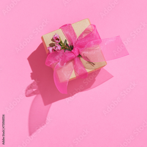 Craft brown gift box with pink ribbon and waxflowers on pink background