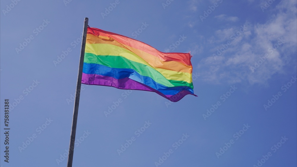 Rainbow LGBT flag waving outdoors with blue sky Rainbow LGBT flag waving outdoors with blue sky