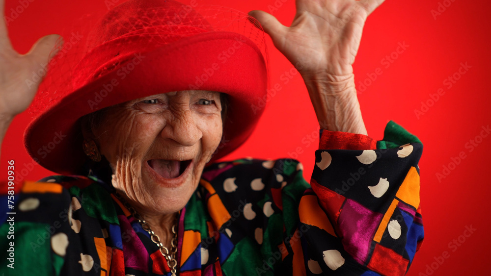 Excited happy fisheye view of funny elderly woman with red hat and no teeth isolated on red background. Excited happy fisheye view of funny elderly woman with red hat and no teeth isolated on red background.
