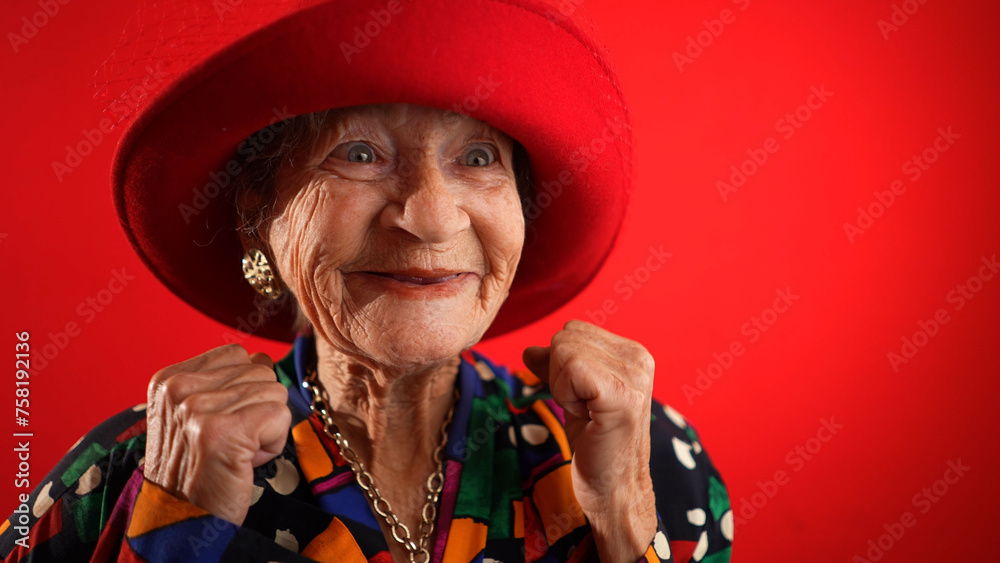 Funny elderly senior old woman with no teeth and wrinkled skin gives great idea gesture showing explosion of thinking posing isolated on red background