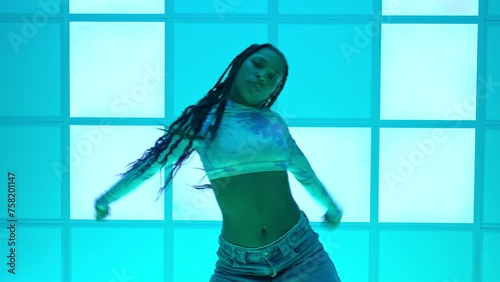 A beautiful Latin girl, African American, dances hip hop music in front of a neon blue background.
Concept of energy, freedom and love for music