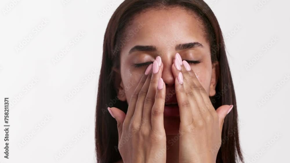 A serene woman with her eyes closed, gently touching her face while applying cosmetic cream under her eyes A serene woman with her eyes closed, gently touching her face while applying cosmetic cream under her eyes