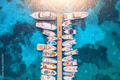 Aerial view of boats and luxure yachts in dock at sunset in summer in Sardinia, Italy. Colorful landscape with sailboats and motorboats in sea bay, jatty, clear blue sea. Top view of harbor. Travel photo