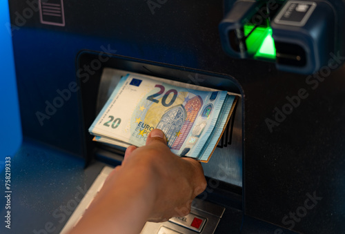 Close up of hand of unrecognizable person taking out money in twenty euro bills from an ATM in airport