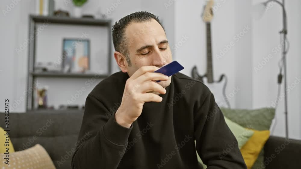 A contemplative man holds a credit card at home, reflecting on finance or online shopping. A contemplative man holds a credit card at home, reflecting on finance or online shopping.