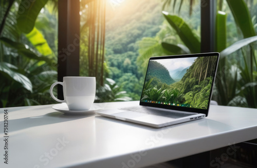 Laptop and coffee cup on white table with green nature background.