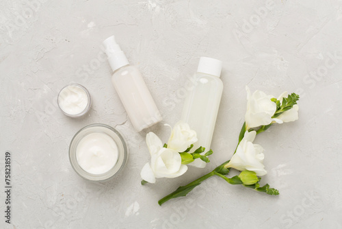 Facial cosmetic products with freesia flowers on concrete background, top view