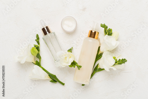 Facial cosmetic products with freesia flowers on concrete background, top view