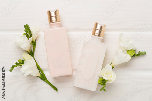 Facial cosmetic products with freesia flowers on wooden background, top view