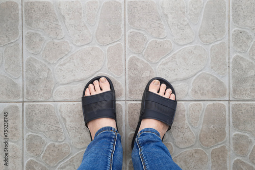 Legs in black pool sandals and jeans on tiled floor. Selfie from personal perspective. View from above on feet in pool flip-flops.