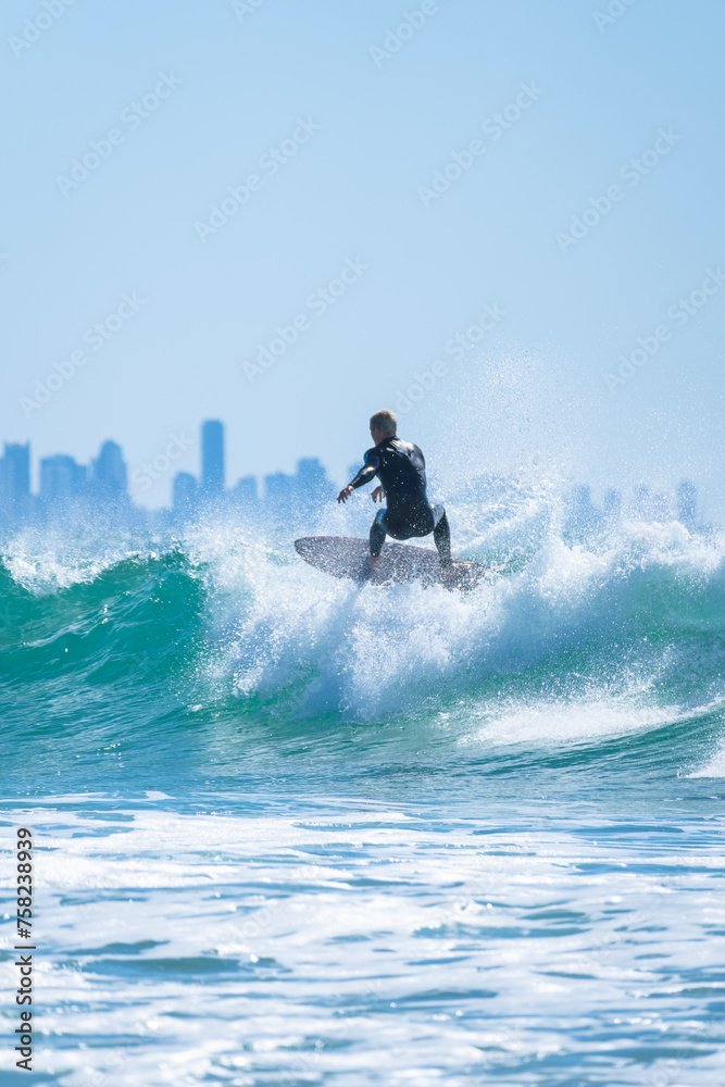 Naklejka premium Professional surfer in black wetsuit riding a wave on the city beach