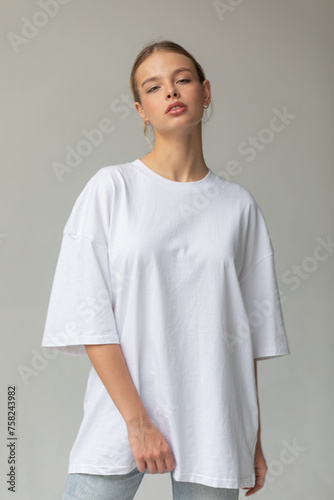 Beautiful blonde girl in a white oversized T-shirt and blue jeans posing on a gray background