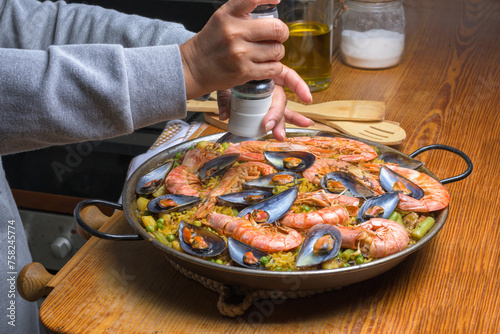 Person seasoning a paella with prawns and mussels, evoking home cooking, typical Spanish cuisine, Majorca, Balearic Islands, Spain