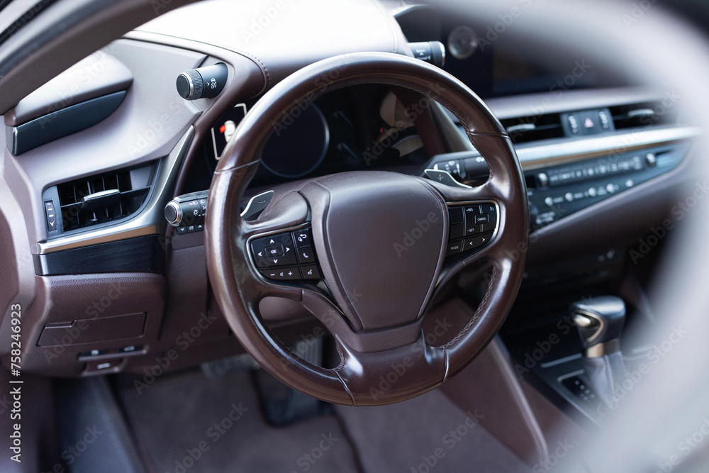 Car steering wheel. Brown leather dashboard, climate control, speedometer, display, wood decoration. Expensive car interior with steering wheel.