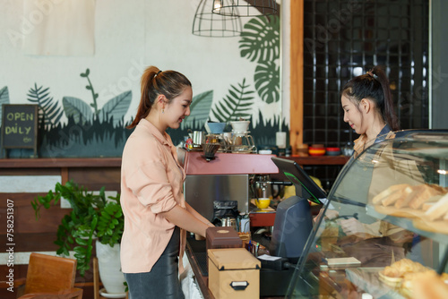  beautiful Asian female customer is ordering coffee and bakery items from beautiful Asian female shopkeeper barista inside cafe Minimalist style cafe shop coffee shop is small business