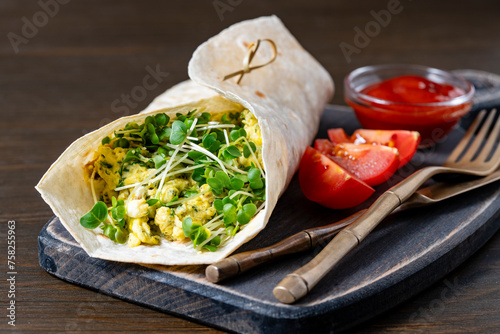Homemade burrito wraps with scrambled egg omelet and microgreens for healthy breakfast on wooden board, closeup