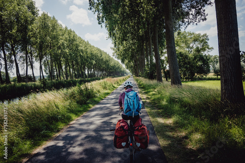 Frau radelt während einer Radreise auf einem Radweg entlang eines Kanals in Flandern, Belgien photo