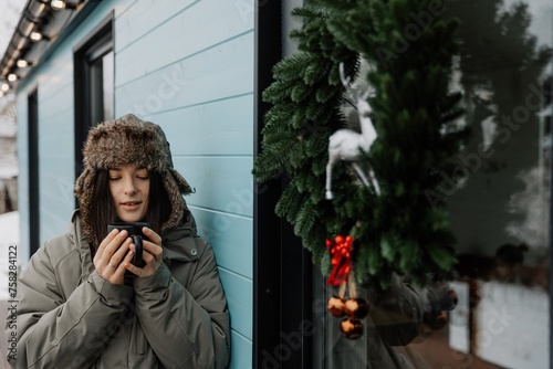 A brunette girl drinks coffee in winter. A young woman  in a hat is having fun in the winter outdour. Lifestyle photo