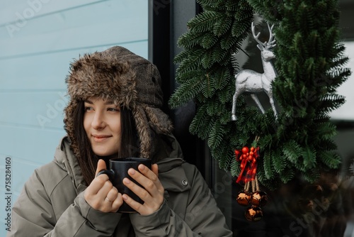 A brunette girl drinks coffee in winter. A young woman  in a hat is having fun in the winter outdour. Lifestyle photo