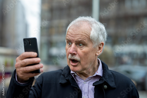 Senior man loocking in shock at his mobile phone. photo