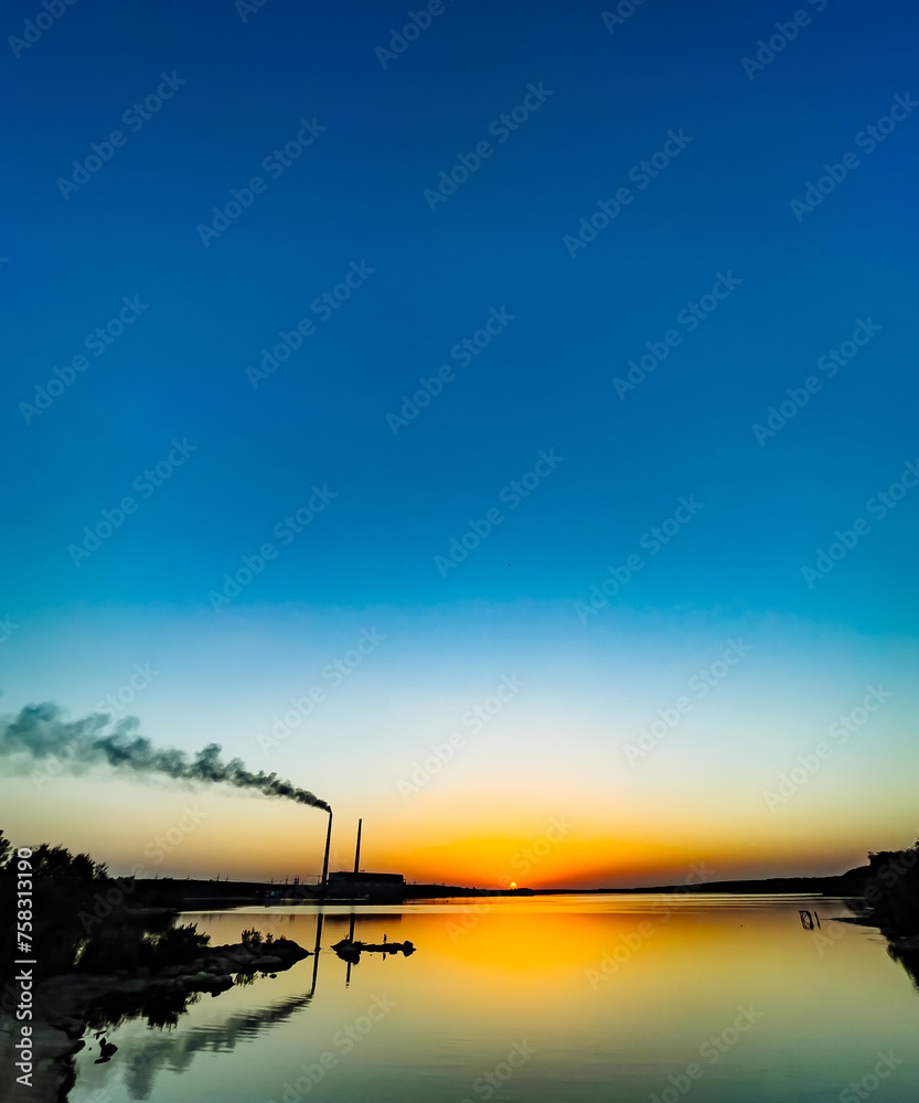 Obraz premium Power plant emits smoke into the air at sunset.