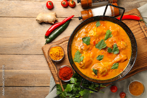 Tasty chicken curry with parsley and ingredients on wooden table, flat lay. Space for text