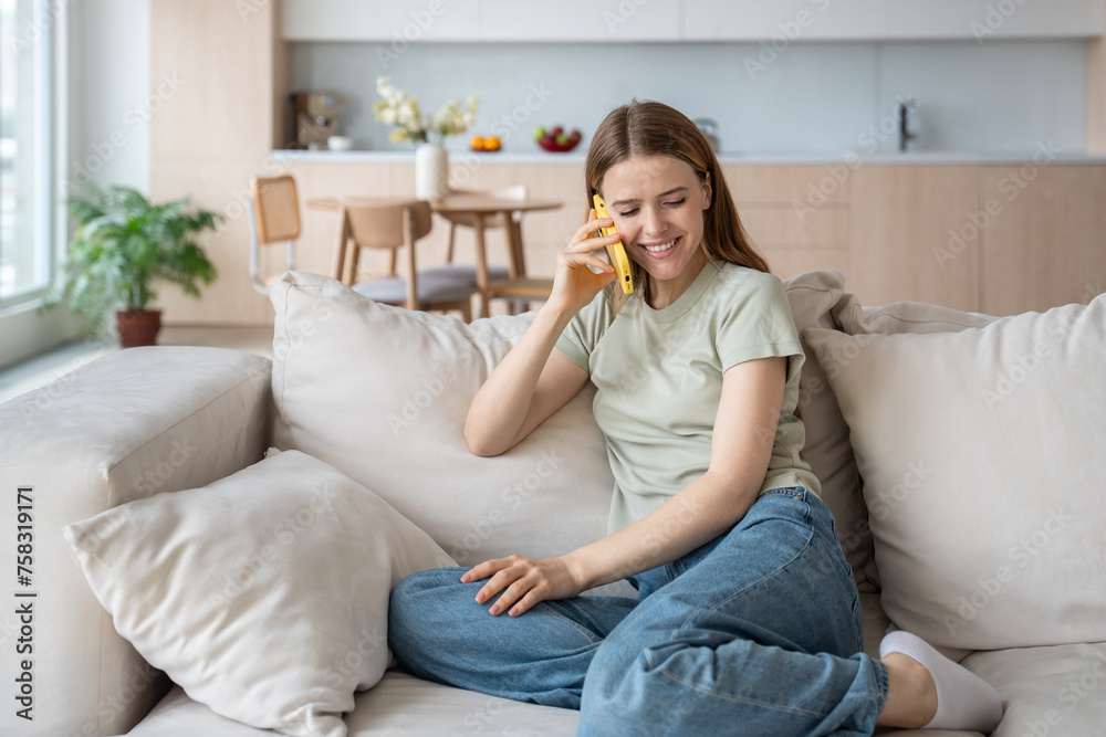 Smiling woman talk on mobile phone while sitting comfortably on sofa in living room. Pleased relaxed female having pleasant warm conversation making smartphone call while learning good news at home. Smiling woman talk on mobile phone while sitting comfortably on sofa in living room. Pleased relaxed female having pleasant warm conversation making smartphone call while learning good news at home.
