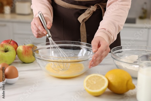 Woman whisking eggs in bowl at light marble table indoors, closeup